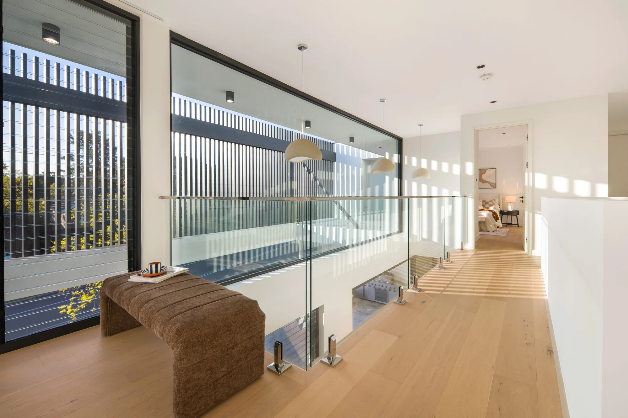 Upper-level passage with a glass balustrade and screened windows overlooking the void